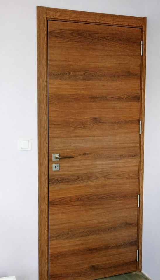 Complete warm wood-effect laminate interior door with full frame, architraves and four hinges visible